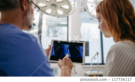 Doctor discussing test resulst with teenage patient, showing data on tablet in emergency room. 117736117