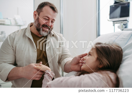 Father beside daughter on hospital bed, holding hands. Sick little girl in hospital. 117736223