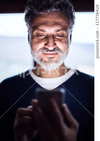Portrait of handsome man looking at smartphone screen. Display glow illuminates man's face. Portrait of handsome man looking at smartphone screen. Display glow illuminates man's face. 117736428