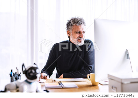 Handsome man working from home office, sitting at desk with computer, smiling. Telecommuting and home office. Handsome man working from home office, sitting at desk with computer, smiling. Telecommuting and home office. 117736442