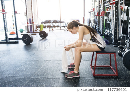 Young fitness girl feeling exhausted after hard workout in gym, sitting on bench, breathing. Young fitness girl feeling exhausted after hard workout in gym, sitting on bench, breathing. 117736601