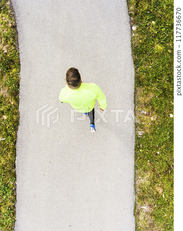 Aerial view of a runner running through autumn park on jogging path. Morning running training. 117736670