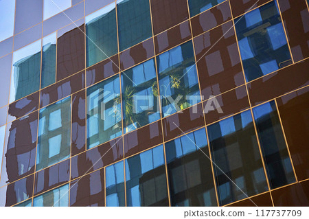 Modern glass office building reflecting city skyline in windows at sunset. Contemporary architectural design Modern glass office building reflecting city skyline in windows at sunset. Contemporary architectural design 117737709