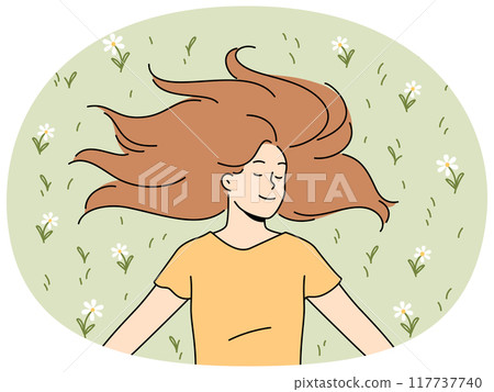 Happy woman with long hair lies on grass in park with eyes closed and smiles rejoicing in sunlight 117737740