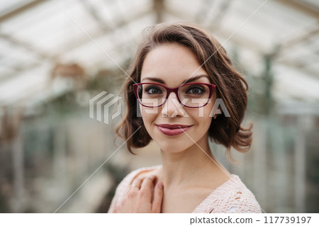 Small greenhouse business. Businesswoman selling flowers and houseplants, standing in greenhouse, looking at camera, smiling. 117739197