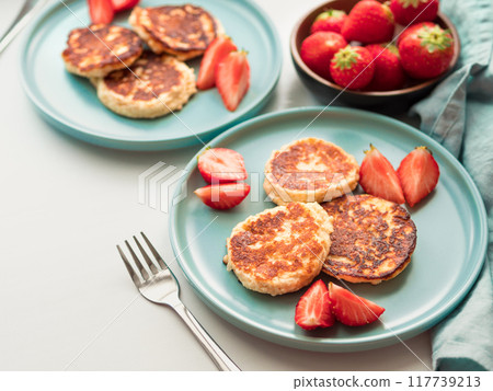 Sweet cheese pancakes on plate served strawberries. Cottage cheese pancakes, syrniki, ricotta fritters, curd fritters, Copy space for text or design. Sweet cheese pancakes on plate served strawberries. Cottage cheese pancakes, syrniki, ricotta fritters, curd fritters, Copy space for text or design. 117739213