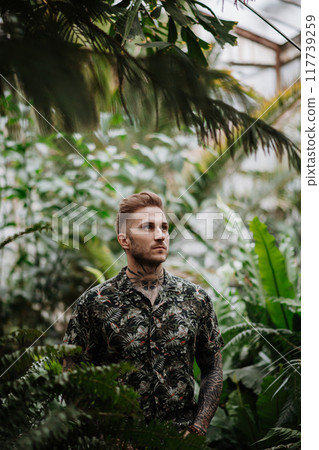 Handsome man with tattoo standing in botanical garden, in the middle of lush green foliage. Handsome man with tattoo standing in botanical garden, in the middle of lush green foliage. 117739259