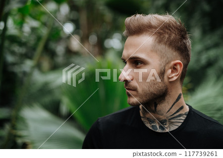Handsome man with tattoo standing in botanical garden, in the middle of lush green foliage. Handsome man with tattoo standing in botanical garden, in the middle of lush green foliage. 117739261