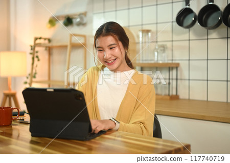 Happy young asian woman working on digital tablet at a kitchen counter Happy young asian woman working on digital tablet at a kitchen counter 117740719