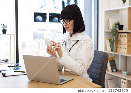 Female doctor working with laptop and holding medicine bottle 117743829