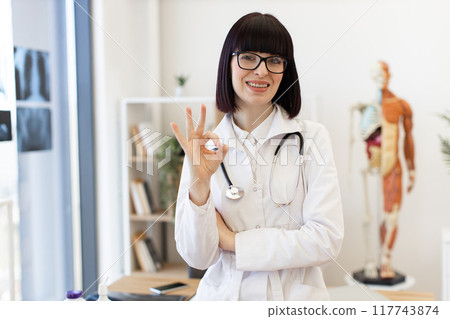 Confident female doctor giving ok sign in medical office Confident female doctor giving ok sign in medical office 117743874