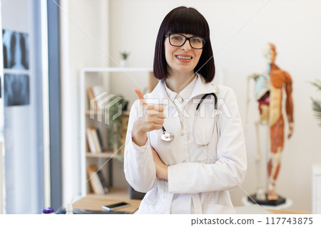 Confident female doctor giving thumbs up in medical office Confident female doctor giving thumbs up in medical office 117743875