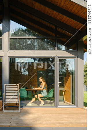 Woman working at a computer in a modern country house with a large glass facade in sunny day 117744741