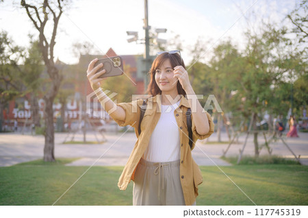 Traveler asian woman in her 30s making a livestream or selfie with a smartphone in evening scene while solo travel in Bangkok, Thailand. Traveler asian woman in her 30s making a livestream or selfie with a smartphone in evening scene while solo travel in Bangkok, Thailand. 117745319