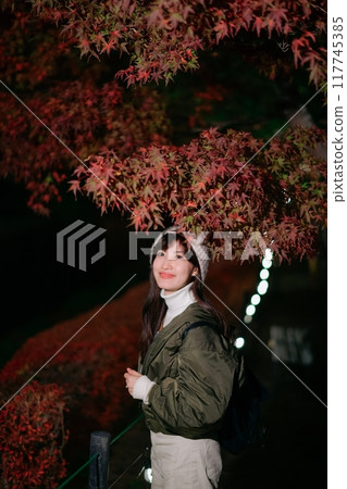 Asian woman in a chic jacket, experiencing the magic of Christmas in Japan's urban night. A festive portrait amidst snow and nature's vibrant beauty. 117745385