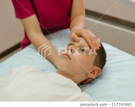 Osteopathy Treatment. Boy's forehead being manipulated by real osteopathic physician. Naturopath treats kid with osteopathy as alternative medicine and therapy. Osteopath harmonizes body Osteopathy Treatment. Boy's forehead being manipulated by real osteopathic physician. Naturopath treats kid with osteopathy as alternative medicine and therapy. Osteopath harmonizes body 117745863