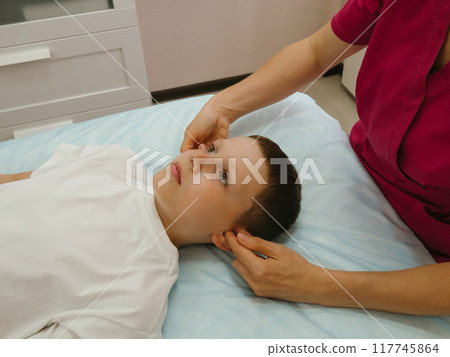 Osteopathy Treatment. Boy's ears being manipulated by real osteopathic physician. Naturopath treats kid with osteopathy as alternative medicine and therapy. Osteopath harmonizes body 117745864