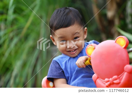 Asian boy about two years old wear a blue shirt was sitting on his toy car. 117746012