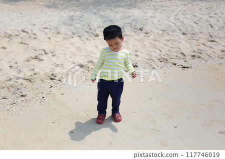 Asian boy about two years old wearing a long-sleeved shirt stand on the beach. 117746019