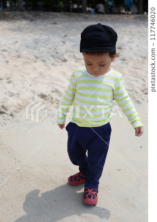 Asian boy about two years old wearing a long-sleeved shirt stand on the beach. 117746020