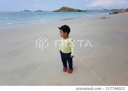A boy about two years old was wearing a long-sleeved shirt standing on the beach. 117746022