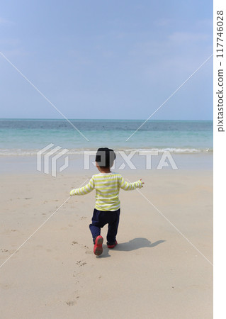 A boy about two years old was wearing a long-sleeved shirt standing on the beach. 117746028