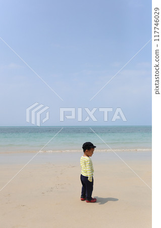 A boy about two years old was wearing a long-sleeved shirt standing on the beach. 117746029