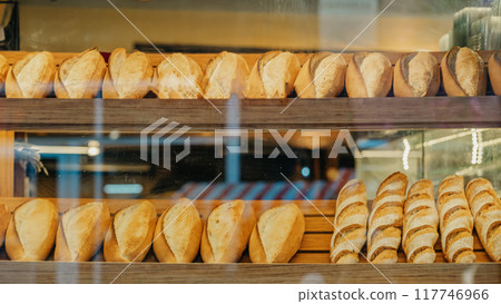 Freshly baked loaves of bread neatly arranged on wooden shelves in bakery Freshly baked loaves of bread neatly arranged on wooden shelves in bakery 117746966