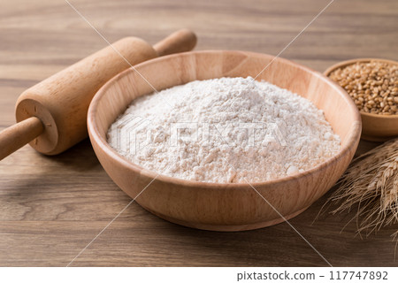 Wheat flour in bowl with wheat grain and rolling pin on wooden background, Food ingredient 117747892