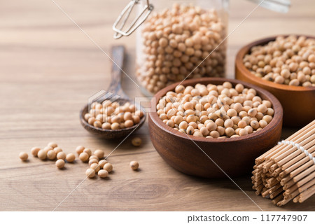 Soy bean seeds in wooden bowl, glass jar and spoon on wooden background Soy bean seeds in wooden bowl, glass jar and spoon on wooden background 117747907