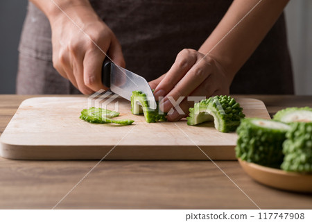 Hand holding kitchen knife and slice bitter gourd on cutting wooden board, Homemade cooking Hand holding kitchen knife and slice bitter gourd on cutting wooden board, Homemade cooking 117747908