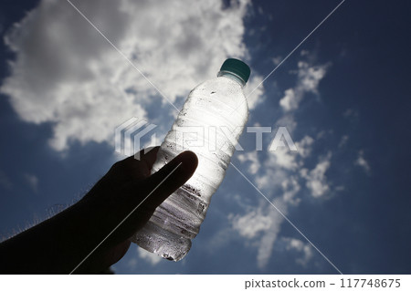 Hand holding a plastic bottle against the blue sky Hand holding a plastic bottle against the blue sky 117748675