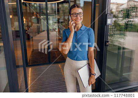 A confident woman uses her smartphone in a modern office, showcasing her elegance and intelligence A confident woman uses her smartphone in a modern office, showcasing her elegance and intelligence 117748801