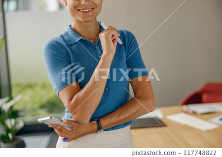 A Confident and Professional Individual in a Contemporary Office Setting with a Smartphone at Hand 117748822