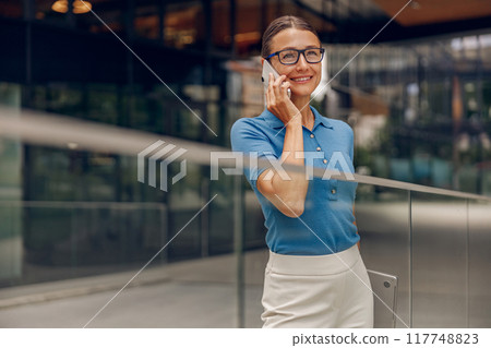 A professional businesswoman is engaged in a phone conversation within a modern office setting A professional businesswoman is engaged in a phone conversation within a modern office setting 117748823