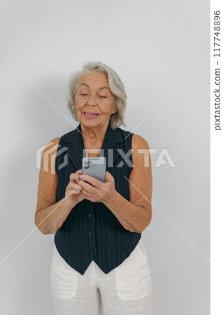 An Elderly Woman Engaged with a Smartphone While Wearing Casual Attire and Accessories 117748896