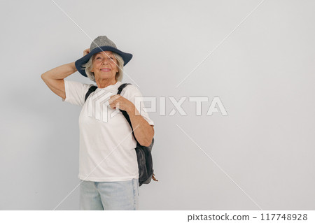 A Senior Woman Wearing a Backpack and a Hat Posed Gracefully in a Minimalist Setting A Senior Woman Wearing a Backpack and a Hat Posed Gracefully in a Minimalist Setting 117748928