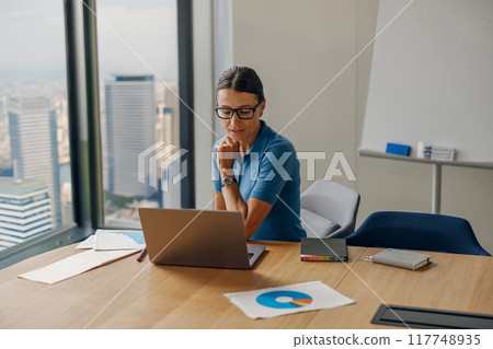 A focused businesswoman is diligently working on her laptop in a modern office environment 117748935