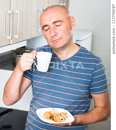 Guy with eyes closed drinking coffee and croissants in the morning Guy with eyes closed drinking coffee and croissants in the morning 117749287