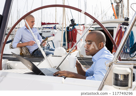Latin American guy with laptop on private yachts in the seaport Latin American guy with laptop on private yachts in the seaport 117749296
