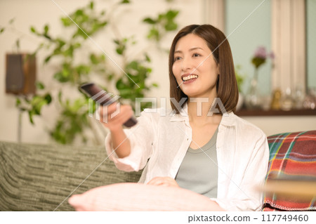 Middle-aged woman relaxing on the sofa and watching TV Middle-aged woman relaxing on the sofa and watching TV 117749460