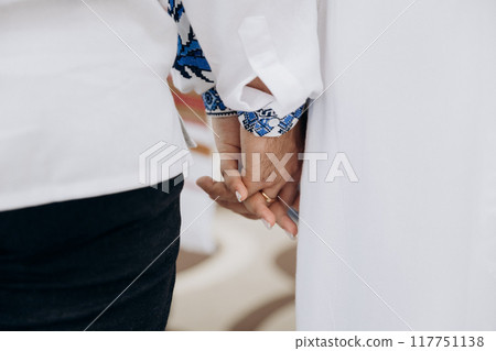 Bride and groom in Ukrainian style clothes with bands holding hands during wedding ceremony Bride and groom in Ukrainian style clothes with bands holding hands during wedding ceremony 117751138