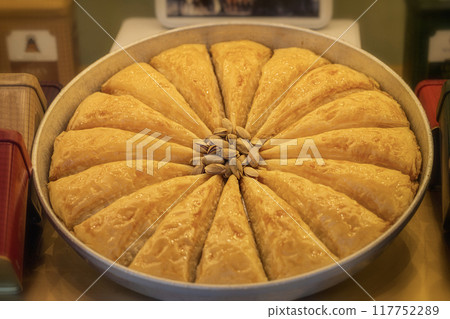 Round tray of baklava, cut into triangular pieces with sprinkle of pistachios on top, local market delight Round tray of baklava, cut into triangular pieces with sprinkle of pistachios on top, local market delight 117752289