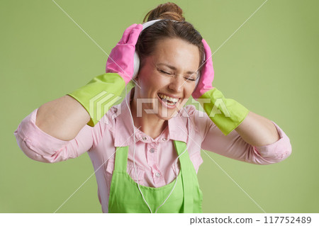 smiling housewife in green apron and rubber gloves on green 117752489