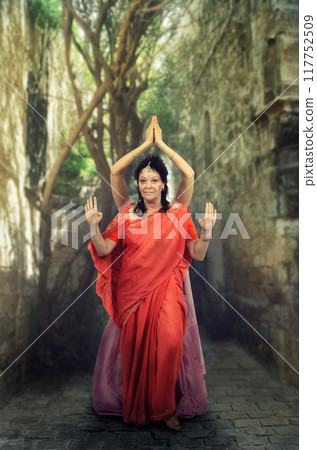 Cultural Dance Performance of Two Women in Orange and Pink Saris on Ancient Pathway, Featuring Bharatanatyam Poses and a Serene, Historical Atmosphere. 117752509
