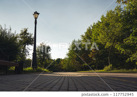 An empty, straight, sidewalk, pedestrian path in the forest park. Street clock An empty, straight, sidewalk, pedestrian path in the forest park. Street clock 117752945