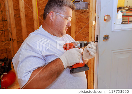 Professional locksmith installing lock doorknob on entrance door of house with screwdriver 117753960