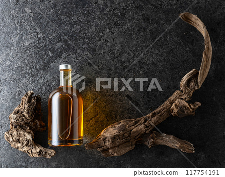 Bottle of whiskey and old snags on a black stone background. 117754191