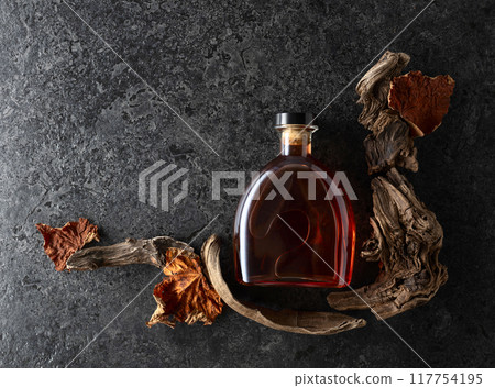Bottle of brandy and old snags with dried up vine leaves. 117754195