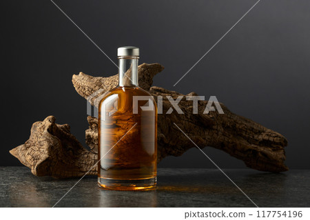 Bottle of whiskey and old snag on a black background. 117754196